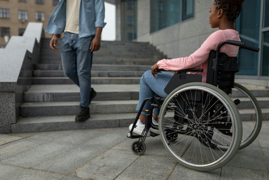 A person in a wheelchair sits at the bottom of a flight of stairs.